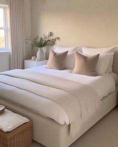 a large white bed sitting in a bedroom next to a window with lots of pillows on it