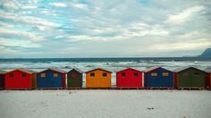 a row of colorful beach huts sitting on top of a sandy beach next to the ocean