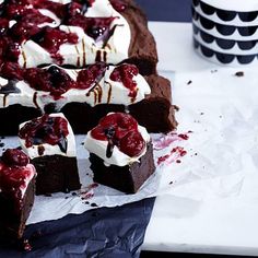 chocolate cake with white frosting and cherries on top sitting on a table next to a teapot