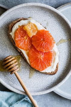 an open face sandwich topped with orange slices and whipped cream on a plate next to a honey comb