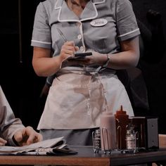 two women in aprons are sitting at a table and one is holding a cell phone