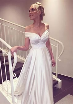 a woman in a white wedding dress standing on stairs with her hand on the rail