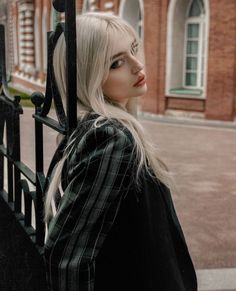 a woman with long blonde hair standing next to a fence