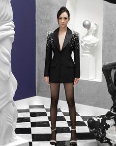 a woman standing in front of a white sculpture wearing black tights and a blazer