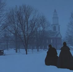 two people sitting in the snow near a church