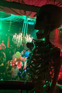 a skeleton standing in front of a green light filled room with many people on the dance floor