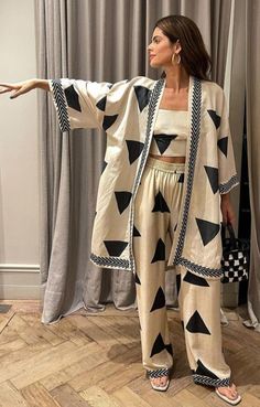 a woman standing in front of a window with her arms spread out and wearing black and white patterned clothing