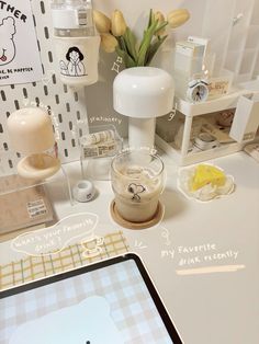 a tablet computer sitting on top of a white desk next to a vase filled with flowers