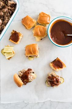 mini sliders with bbq sauce and pickles on parchment paper next to casserole dish