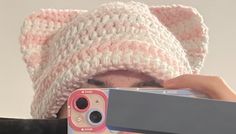 a woman taking a photo with her cell phone while wearing a knitted cat hat