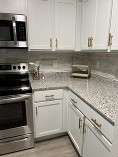 a kitchen with white cabinets, silver appliances and marble counter tops is pictured in this image