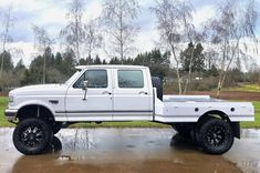 a white pickup truck parked on top of a wet parking lot in front of trees