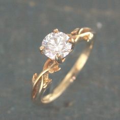 a gold ring with a white diamond in the center and vines on it's side