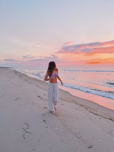 a woman walking on the beach at sunset