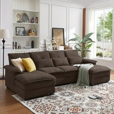 a living room with a large sectional couch and pillows on the floor in front of a window