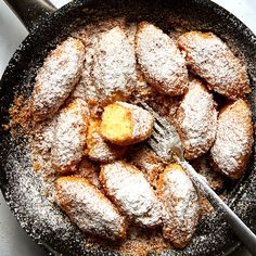 powdered sugar covered pastries are in a skillet with a fork and spoon