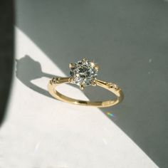 a yellow gold ring with a diamond in the center on a white surface, casting a shadow