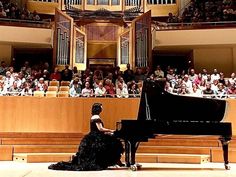 a woman sitting at a piano in front of an auditorium full of people and spectators