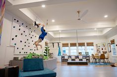 a man is hanging upside down on a climbing wall in a room with chairs and tables