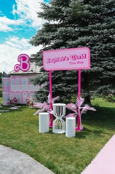 a pink sign sitting in the middle of a lush green field next to a tall tree