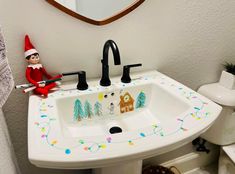 an elf sitting on the edge of a bathroom sink next to a christmas themed faucet