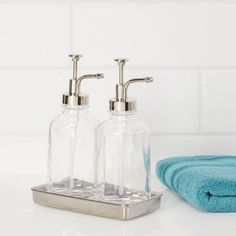 two soap dispensers sitting on top of a counter next to a blue towel