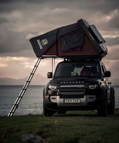 a jeep with a ladder attached to it parked on the grass next to water and mountains