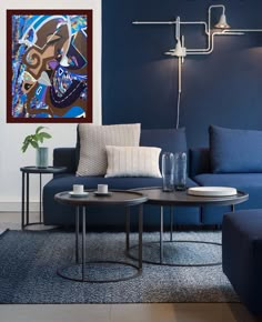 a living room with blue couches and two tables in front of a painting on the wall