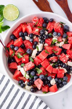 a watermelon salad with blueberries and onions in a white bowl on a marble surface