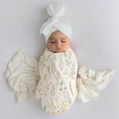 a newborn baby wrapped in a white wrap and wearing a turban headband