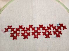 a close up of a cross stitch pattern on a piece of cloth with red thread