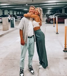 a man and woman hugging each other in an empty parking garage with cars behind them