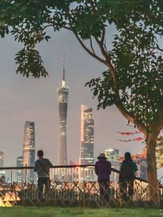 three people are standing on a bridge looking at the cityscape in the distance