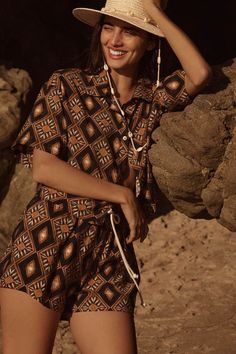 a woman wearing a hat standing next to a rock and holding her hand on her head