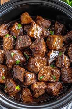 cooked beef cubes in a crock pot with parsley garnish on top