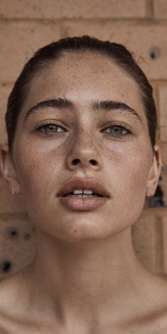 a woman with freckles on her face standing in front of a brick wall