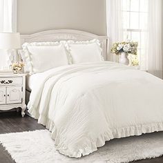 a white bed in a bedroom next to a window with flowers on the side table