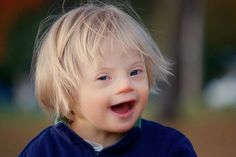 a little boy with blonde hair smiling at the camera