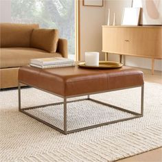 a living room with a couch, coffee table and books on the end table in front of a window