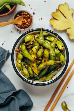 a bowl filled with green peppers next to some chopsticks and other food items