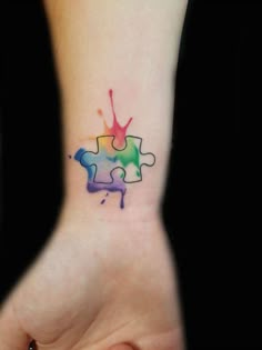 a person's wrist with a colorful puzzle piece tattoo on it