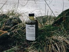 a bottle of liquid sitting on top of grass next to the ocean