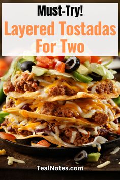 layered tostadas with cheese, olives and other toppings in a cast iron skillet