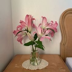 some pink flowers are in a glass vase on a small table next to a bed