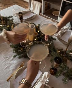 two people holding wine glasses on top of a table with christmas decorations and greenery