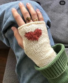 a woman's hand wearing a knitted mitt with a red heart on it