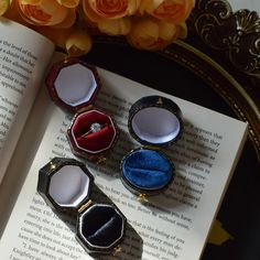 three ring boxes sitting on top of an open book next to flowers and orange roses