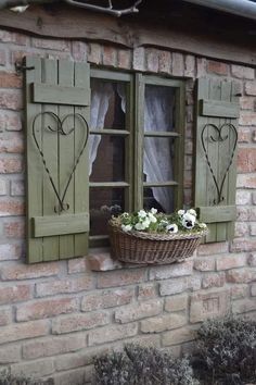 an old brick building with green shutters and flowers in a basket on the window sill