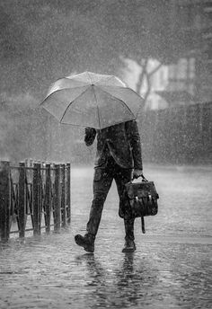 a man walking in the rain with an umbrella over his head while holding a briefcase