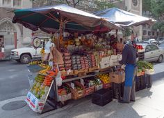 a man standing in front of a fruit stand on the side of a city street